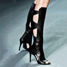 Black high-heeled open-toe leather boots with cutout design, runway fashion footwear, stylish women's knee-high boots, chic modern shoe trend.