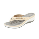 Beige orthopedic wedge sandal with perforated strap, cushioned gray footbed, and decorative metal accent. Comfortable women's footwear.