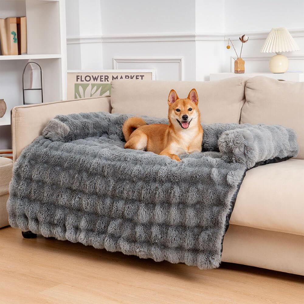 Shiba Inu dog lounging on a plush gray faux fur pet blanket on a beige sofa in a cozy living room setting.