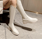 Women's knee-high white leather boots with chunky heels on marble floor, stylish footwear for fashion-forward outfits, elegant and modern design.