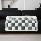 Plush checkered throw blanket in white and gray draped over a black sofa, modern living room decor, cozy home accessory, soft textured design.