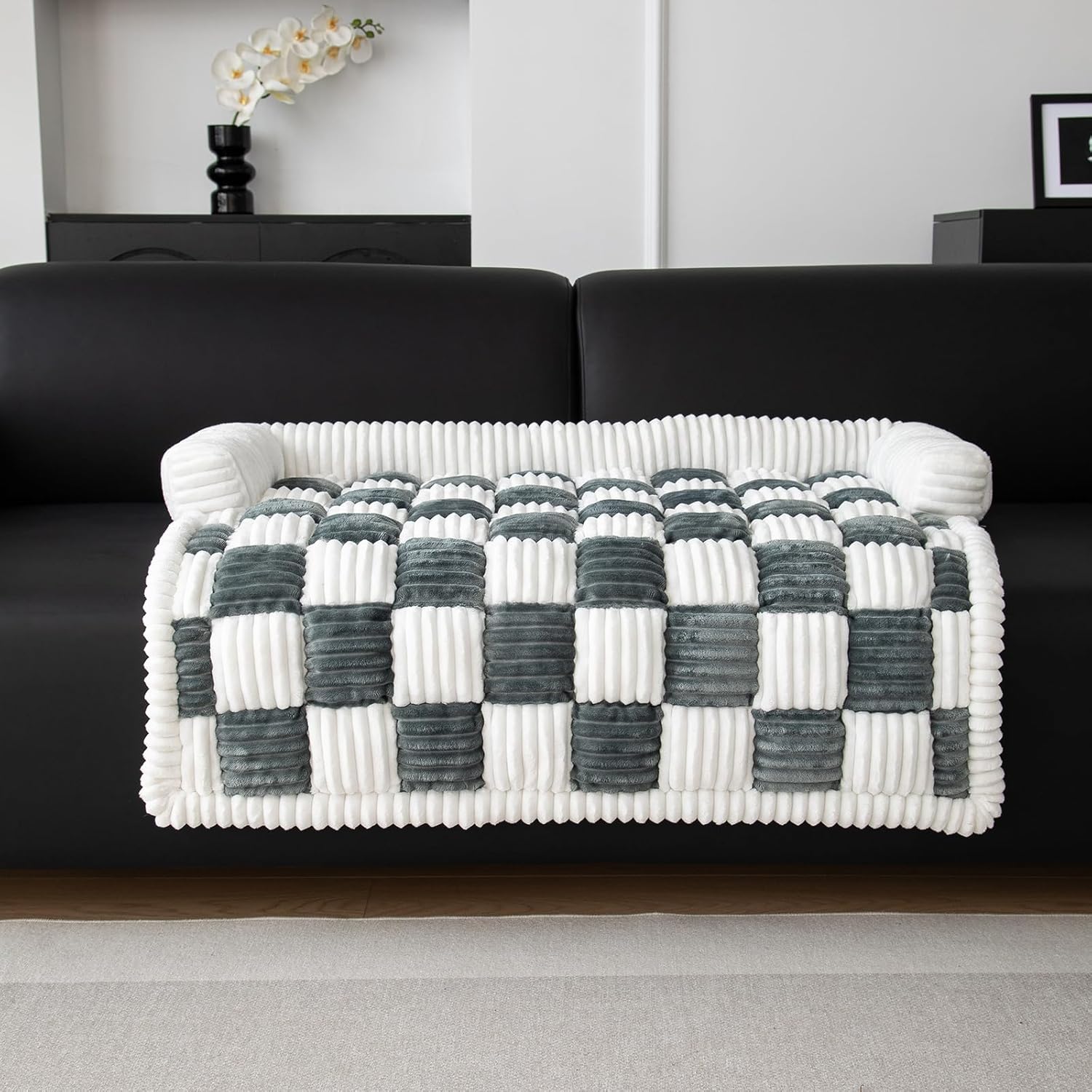 Plush checkered throw blanket in white and gray draped over a black sofa, modern living room decor, cozy home accessory, soft textured design.