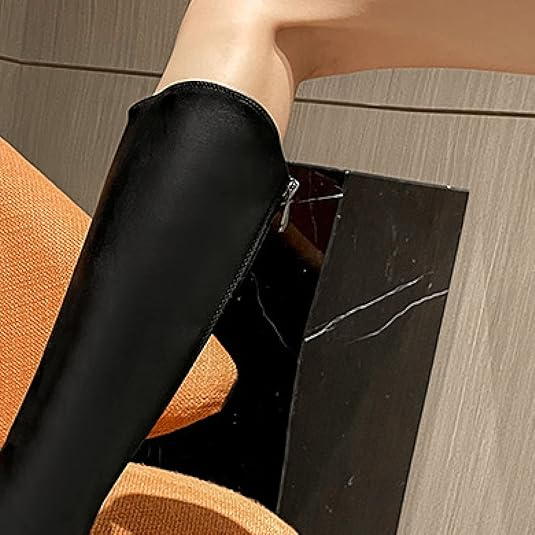 Black leather knee-high boot on a woman's leg, stylish footwear on an orange chair, modern fashion accessory, sleek design, elegant and trendy.