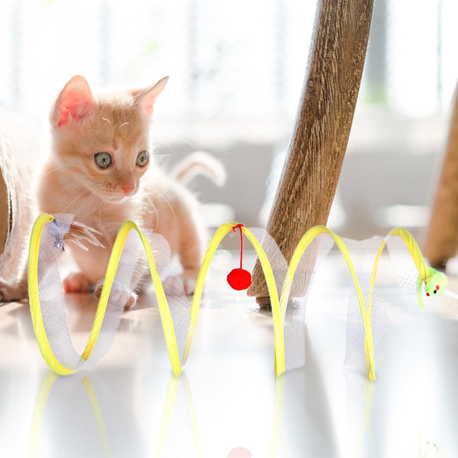 Kitten playing with interactive yellow spiral cat toy featuring red pom-pom and green mouse, perfect for pet entertainment and exercise.