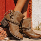 Brown leather ankle boots with stacked heels and wraparound laces, set against a rustic red and white background. Stylish women's footwear.