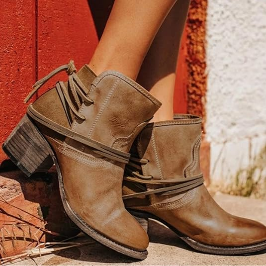 Brown leather ankle boots with stacked heels and wraparound laces, set against a rustic red and white background. Stylish women's footwear.