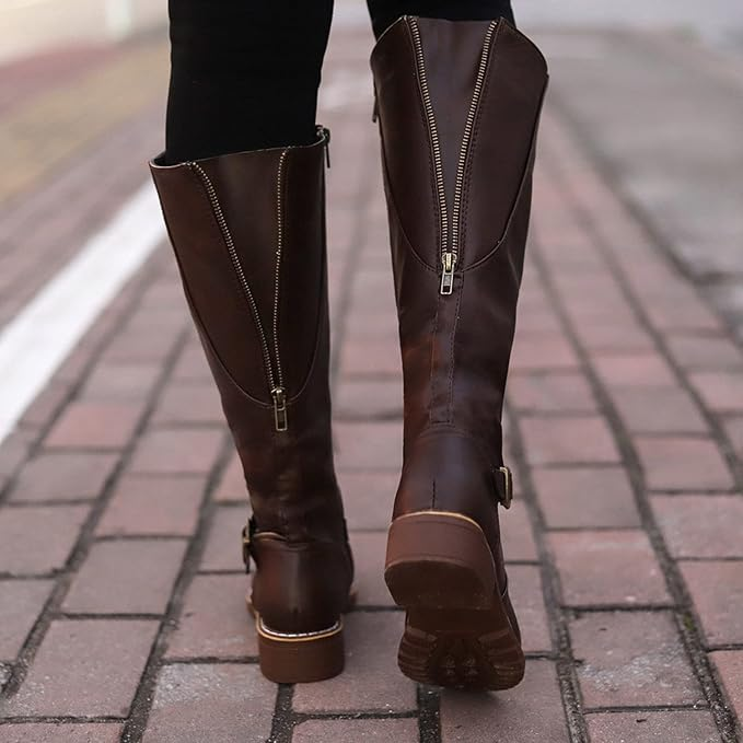 Brown knee-high leather boots with zippers, worn by a person walking on a brick path. Fashionable women's footwear, stylish fall boots.