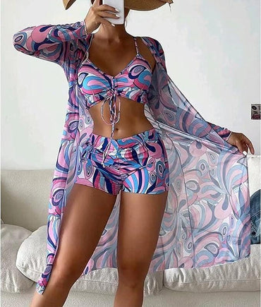 Woman in colorful, abstract-patterned beachwear set with matching cover-up, posing indoors. Fashionable summer outfit, vibrant swimwear style.