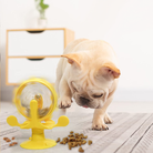 French Bulldog playing with a yellow interactive pet toy on a carpeted floor, with scattered dog food. Pet enrichment, dog toy, playful puppy.