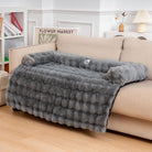 Gray plush pet bed on beige sofa, featuring soft faux fur and raised edges for comfort. Ideal for dogs and cats. Cozy home decor accessory.