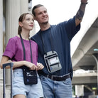 Two people wearing travel neck pouches stand outdoors. The man points ahead, showcasing the convenience of hands-free travel accessories for urban exploration.