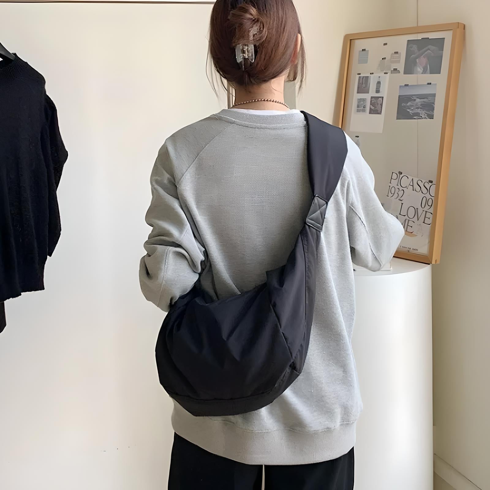 Woman wearing a gray sweatshirt with a black crossbody bag, standing in a modern room with minimalist decor and framed art on the wall.