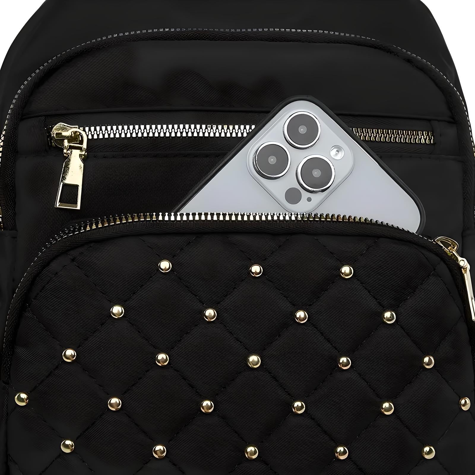 Black quilted backpack with gold studs, featuring a smartphone with triple camera in the front pocket. Stylish accessory for tech-savvy travelers.