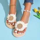 Women's feet wearing beige sandals with large white daisy flowers, paired with anklets, on a light blue background with yellow tulips.