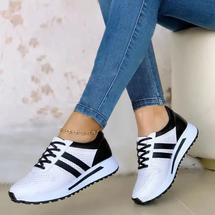 White and black athletic sneakers with perforated design, worn by a person in blue jeans, showcasing casual footwear style.