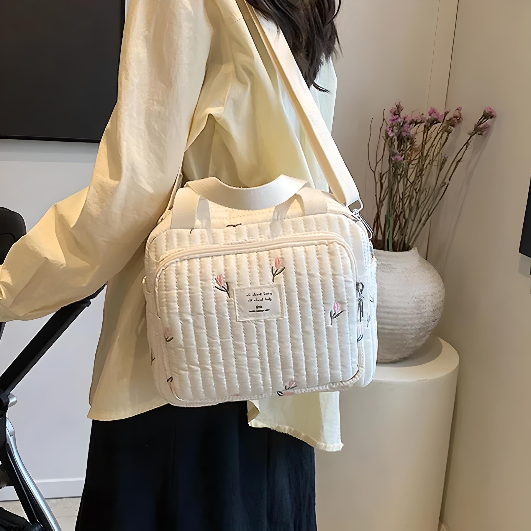 Quilted white shoulder bag with floral embroidery, worn by a person in a casual outfit. Stylish accessory for women, perfect for everyday use.