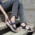 Woman wearing stylish blue orthopedic sandals with thick soles, sitting on concrete steps in casual jeans. Comfortable footwear for outdoor activities.