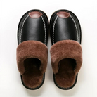 Black leather slippers with brown faux fur lining, featuring white stitching and a slip-on design. Cozy indoor footwear for men and women.