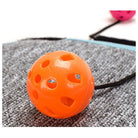 Orange perforated plastic ball toy with string on gray textured surface, ideal for pet play. Durable, interactive pet toy for cats and small dogs.