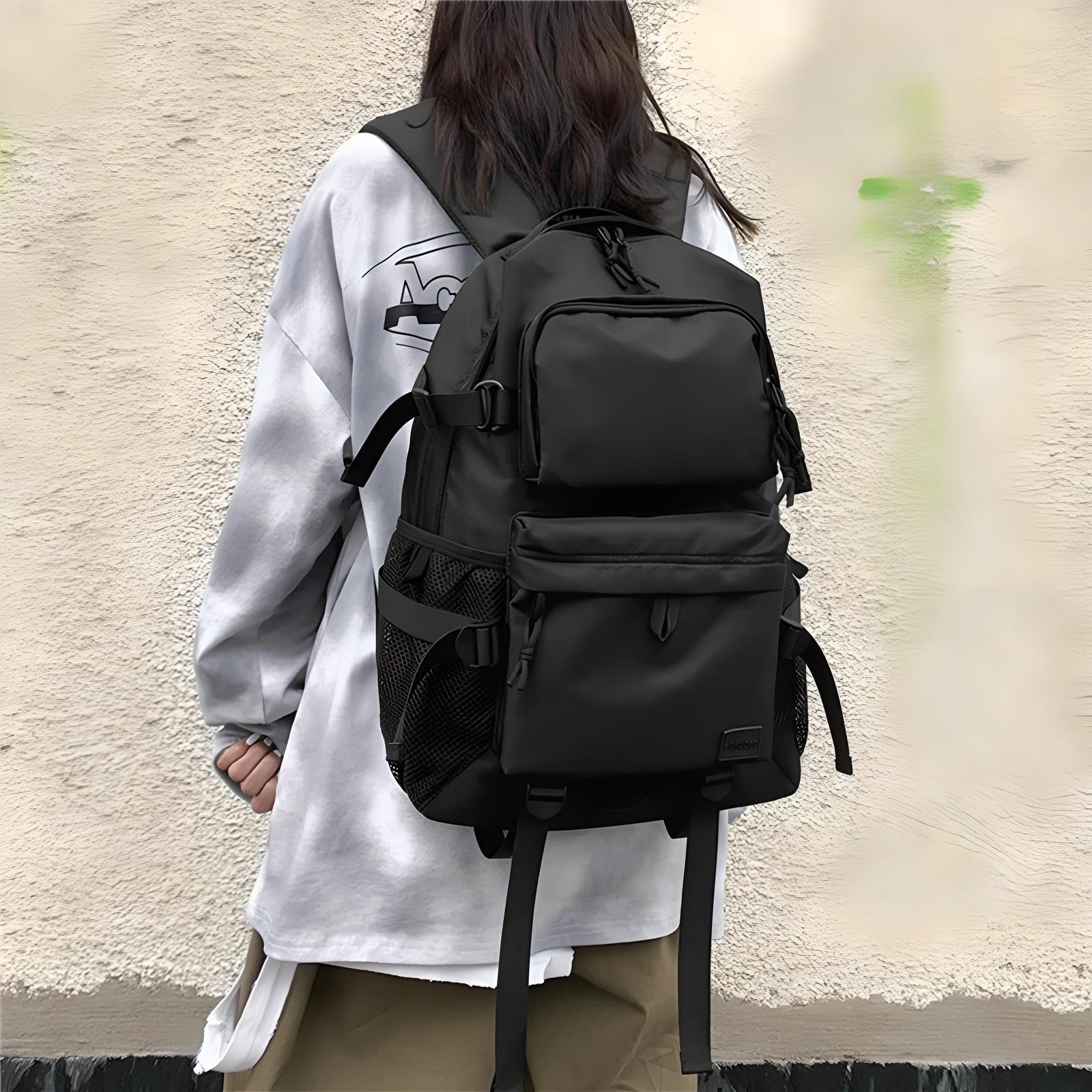 Person wearing a stylish black backpack with multiple compartments and mesh side pockets, ideal for travel and school. Fashionable urban streetwear.