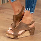 Brown leather wedge sandals with cork platform and stud accents, worn with distressed denim jeans. Fashionable women's summer footwear.