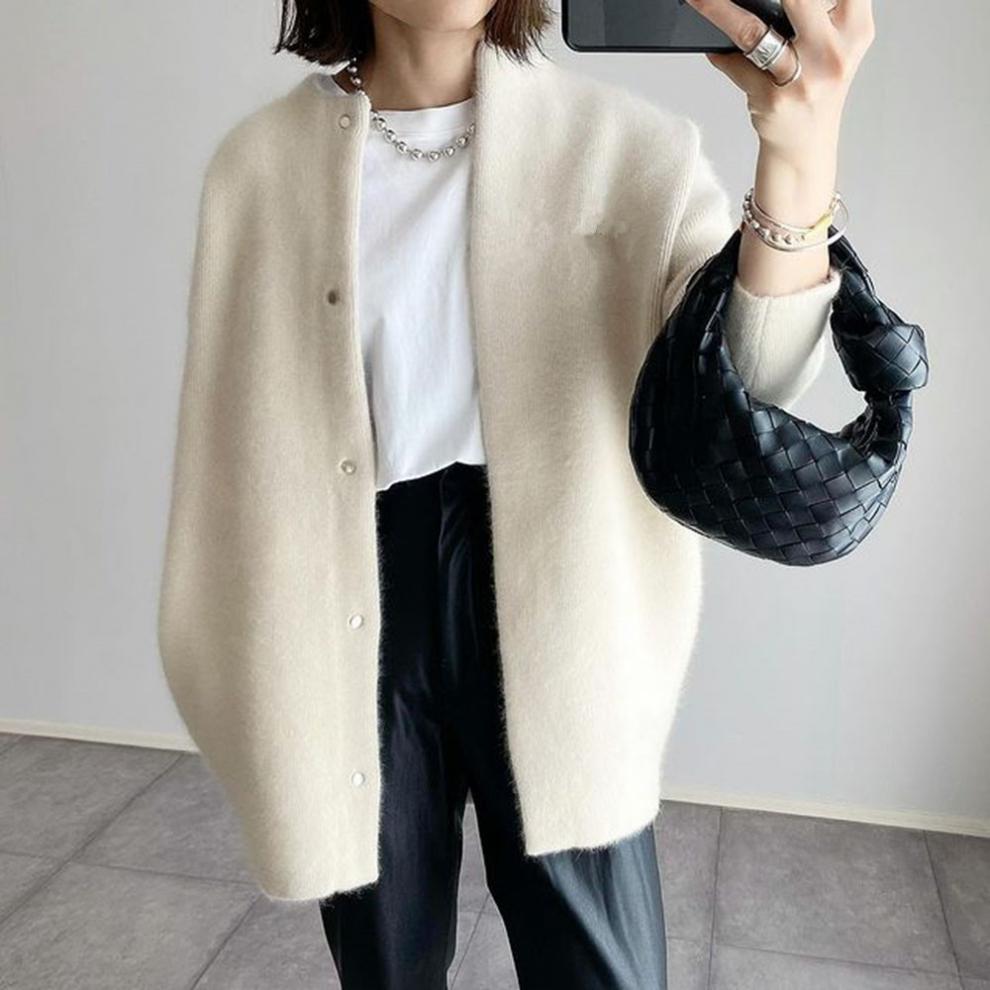 Woman wearing a cream cardigan over a white shirt, holding a black woven handbag. Fashionable outfit with leather pants and silver jewelry.