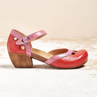 Red leather Mary Jane shoe with pink strap, wooden block heel, and cutout details on a neutral background. Stylish women's footwear, vintage-inspired design.