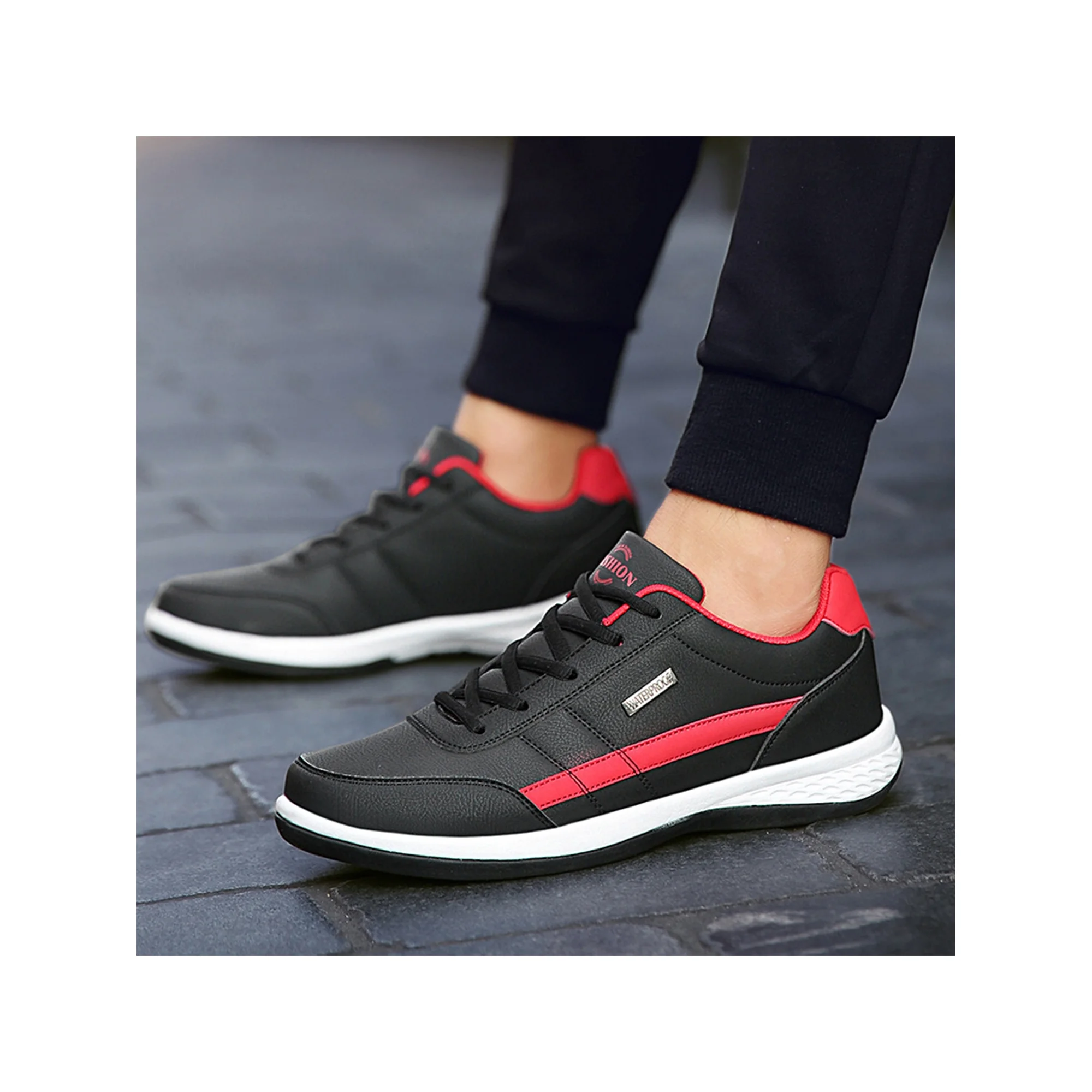 Black and red athletic sneakers with white soles on a cobblestone street, worn with black pants. Stylish men's running shoes, comfortable design.