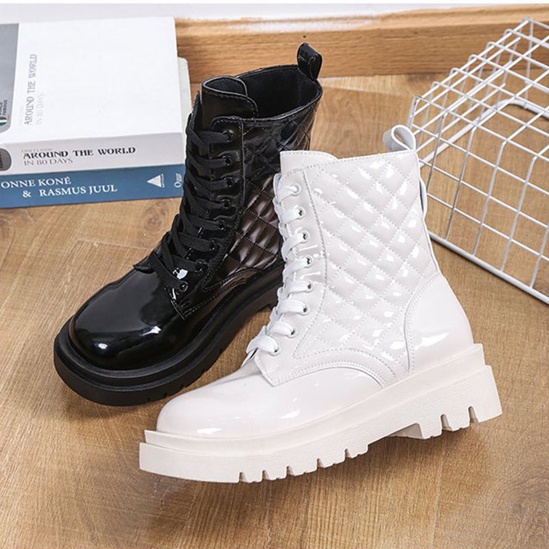 Black and white patent leather combat boots with quilted design on wooden floor, featuring chunky soles and lace-up closure. Fashion footwear.