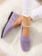 Women's lavender knit loafers on feet with pearl anklet, paired with white ripped jeans, on a fluffy white rug. Fashionable casual footwear.