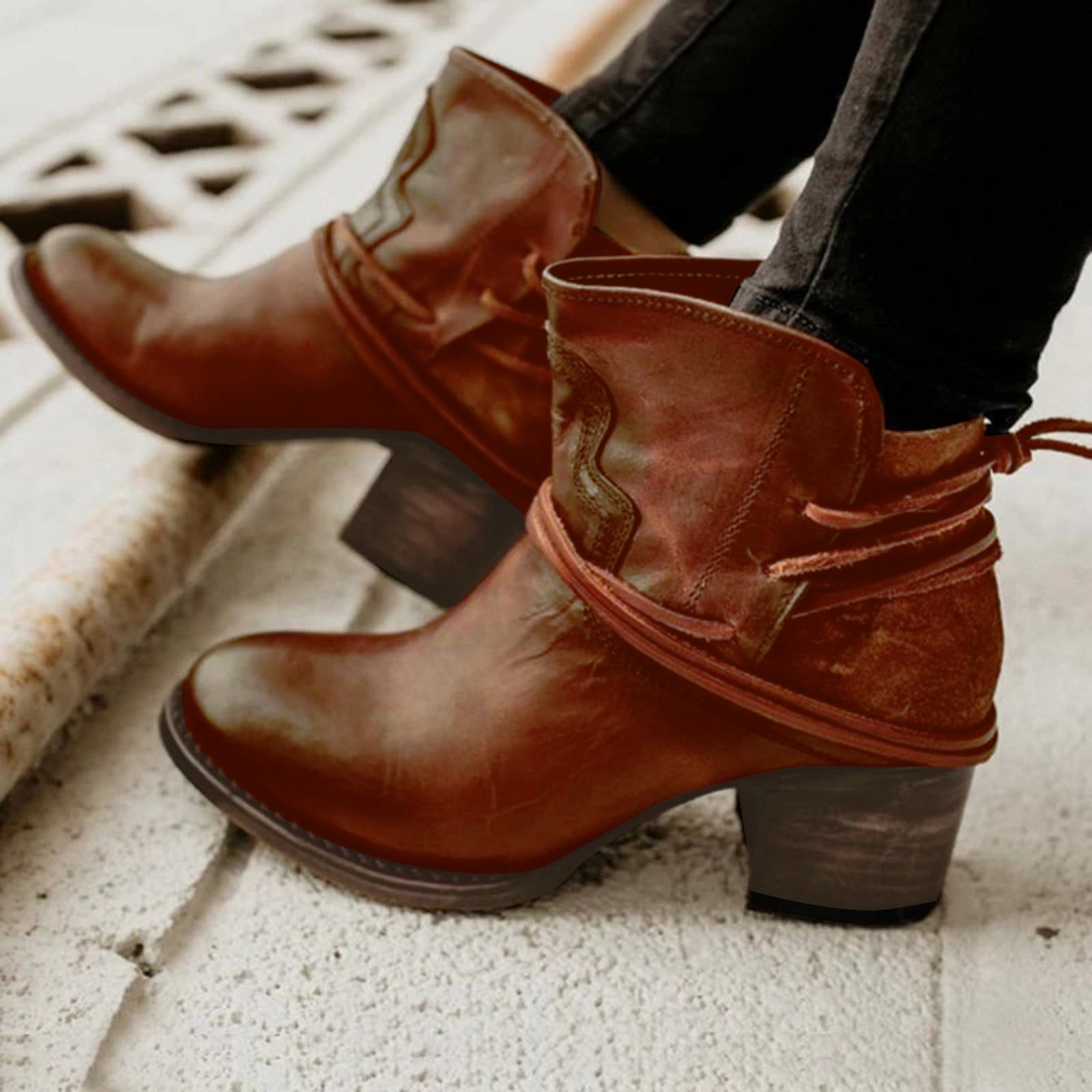 Brown leather ankle boots with block heels and decorative straps, worn with black jeans. Stylish women's footwear for casual and trendy outfits.