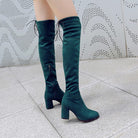 Emerald green knee-high boots with block heels and lace-up detail, stylish women's footwear on tiled floor, perfect for fashion-forward outfits.