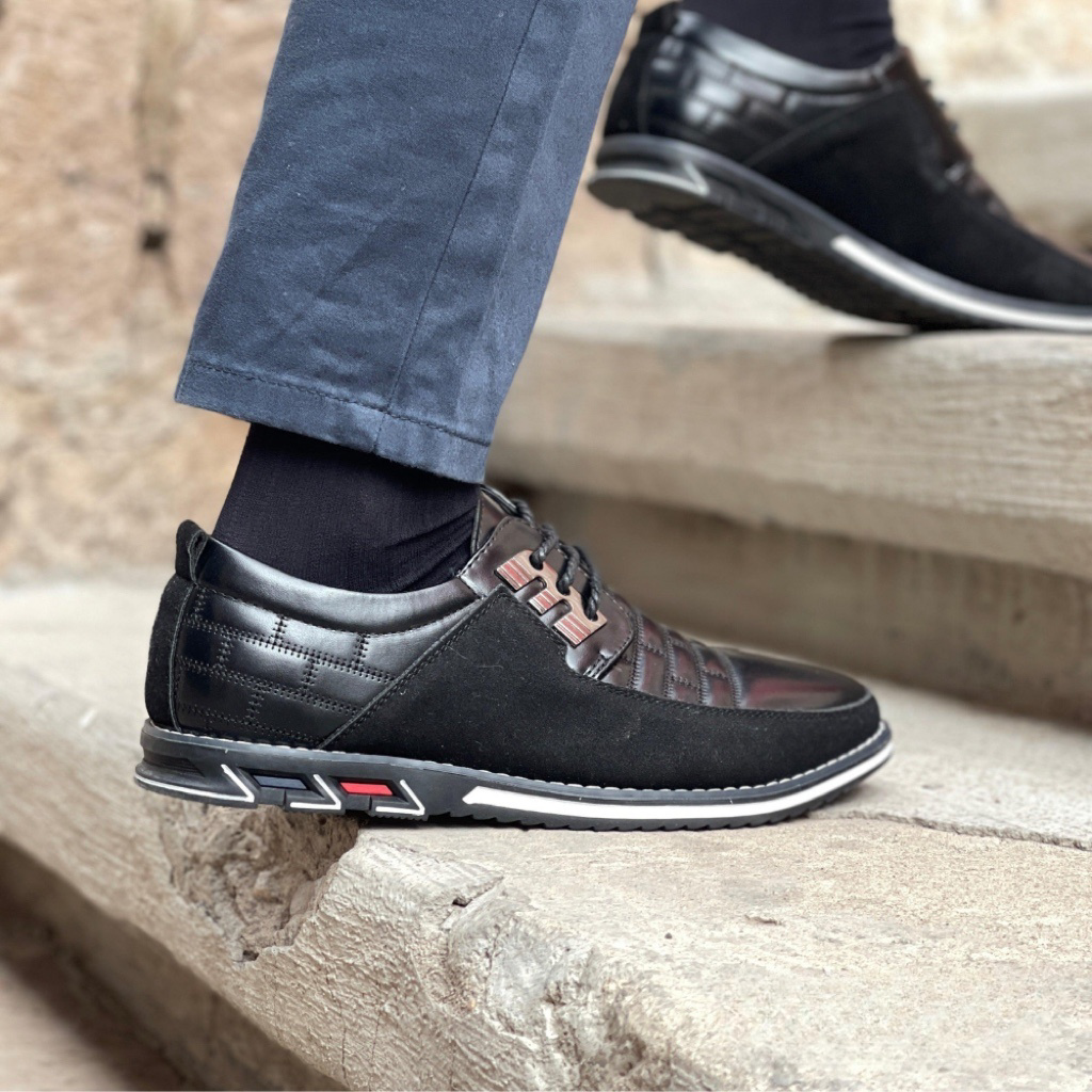 Men's stylish black leather sneakers with red accents, worn with navy pants, stepping on stone stairs. Fashionable casual footwear for men.