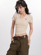 Woman wearing a beige fitted V-neck t-shirt and olive cargo pants, accessorized with a brown belt and hair clip, posing against a white background.