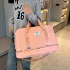 Woman holding a stylish pink quilted duffel bag with shoulder straps, wearing a casual grey sweatshirt and jeans. Perfect for travel or gym use.