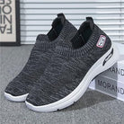 Black slip-on sneakers with white soles, featuring a knit design and logo patch. Comfortable, lightweight footwear ideal for casual wear and walking.