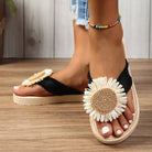 Women's black sandals with white daisy flower embellishment, platform sole, and beaded anklet on wooden floor. Summer footwear fashion.