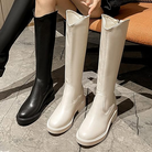 Stylish knee-high boots in black and white leather on a marble floor, showcasing modern fashion footwear trends for women.