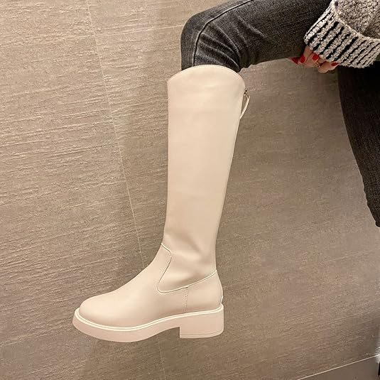 White knee-high leather boot with chunky heel, worn with gray jeans and a knit sweater. Stylish women's footwear, fashion-forward design.