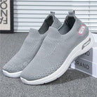 Gray slip-on athletic sneakers with knit upper, cushioned sole, and logo detail, ideal for running and casual wear. Comfortable, lightweight design.