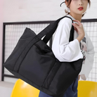 Woman carrying large black tote bag, perfect for travel or gym use. Stylish, spacious, and durable design. Ideal for fashion and utility.