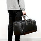 Man holding stylish black leather duffel bag with brown accents, perfect for travel or gym use. Durable, spacious, and fashionable accessory.