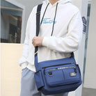 Man wearing white hoodie and blue pants carrying a stylish blue crossbody bag with multiple zippered compartments, ideal for casual fashion and travel.