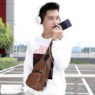 Man wearing headphones and a white sweater with a geometric design, holding a smartphone, and carrying a brown leather crossbody bag outdoors.