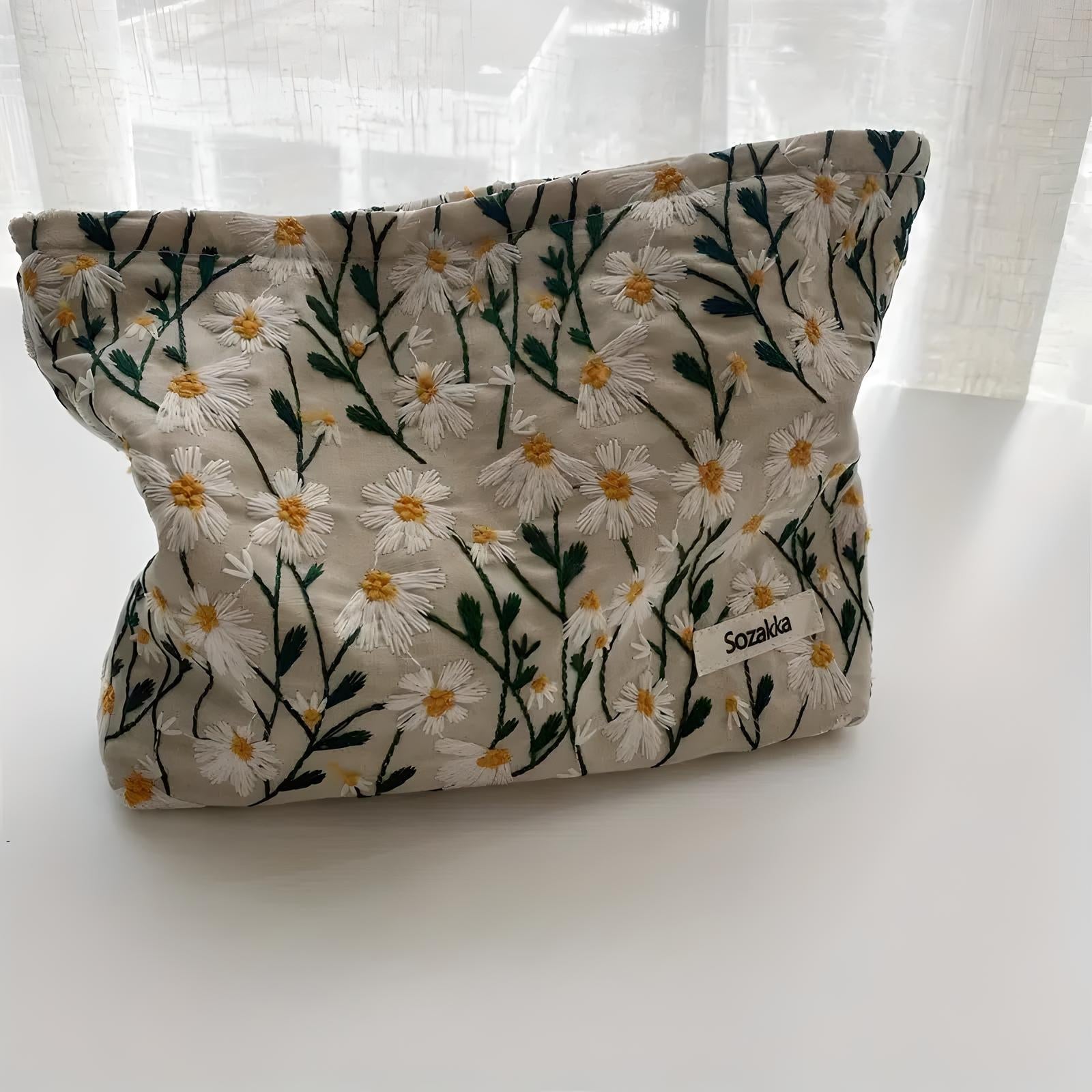 Floral embroidered fabric pouch with daisy pattern on a white background, featuring a "Sozaka" label. Perfect for stylish storage and travel.