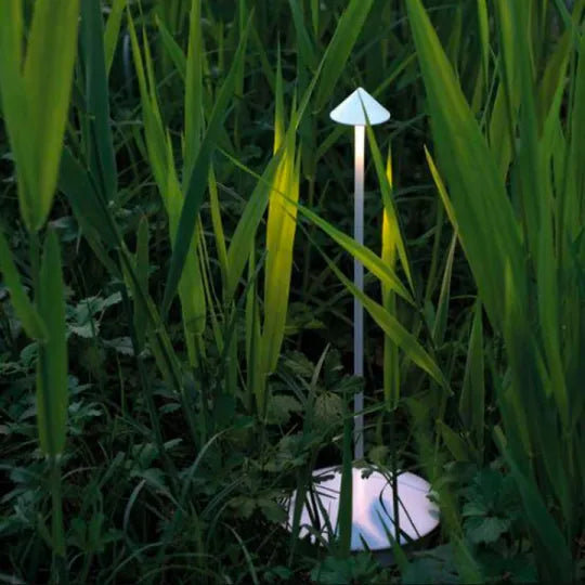 Modern outdoor garden lamp resembling a mushroom, surrounded by tall green grass, providing ambient lighting. Ideal for eco-friendly landscape design.