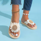 Women's white daisy sandals with braided straps, gold anklet, and white toenail polish on a blue background. Summer fashion footwear.