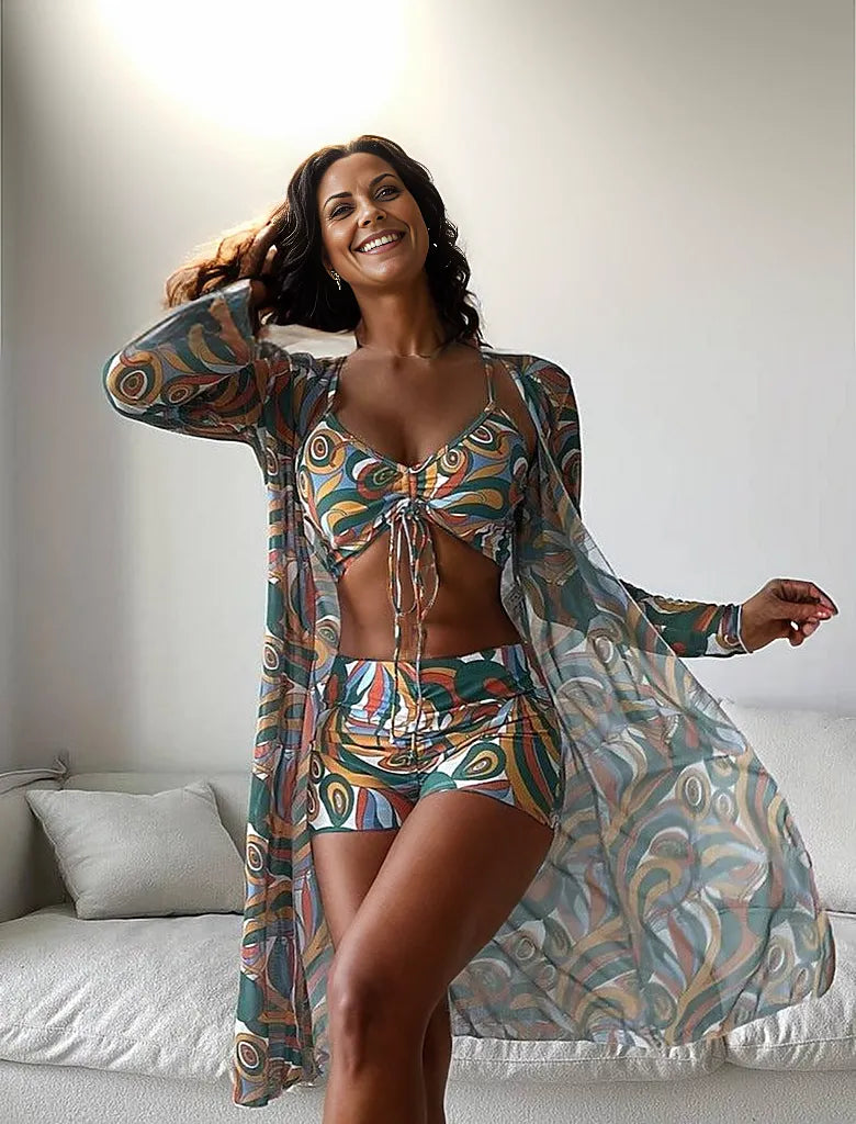 Woman in colorful patterned beachwear set, including a bikini top, shorts, and sheer cover-up, standing indoors. Fashionable summer outfit.