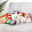 White Pomeranian dog on a gray sofa surrounded by colorful plush potato chip pillows, indoor setting, cute pet, cozy home decor.