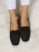 Black rhinestone loafers on white fur rug, featuring pearl anklet and distressed white jeans. Stylish women's footwear, elegant and trendy design.